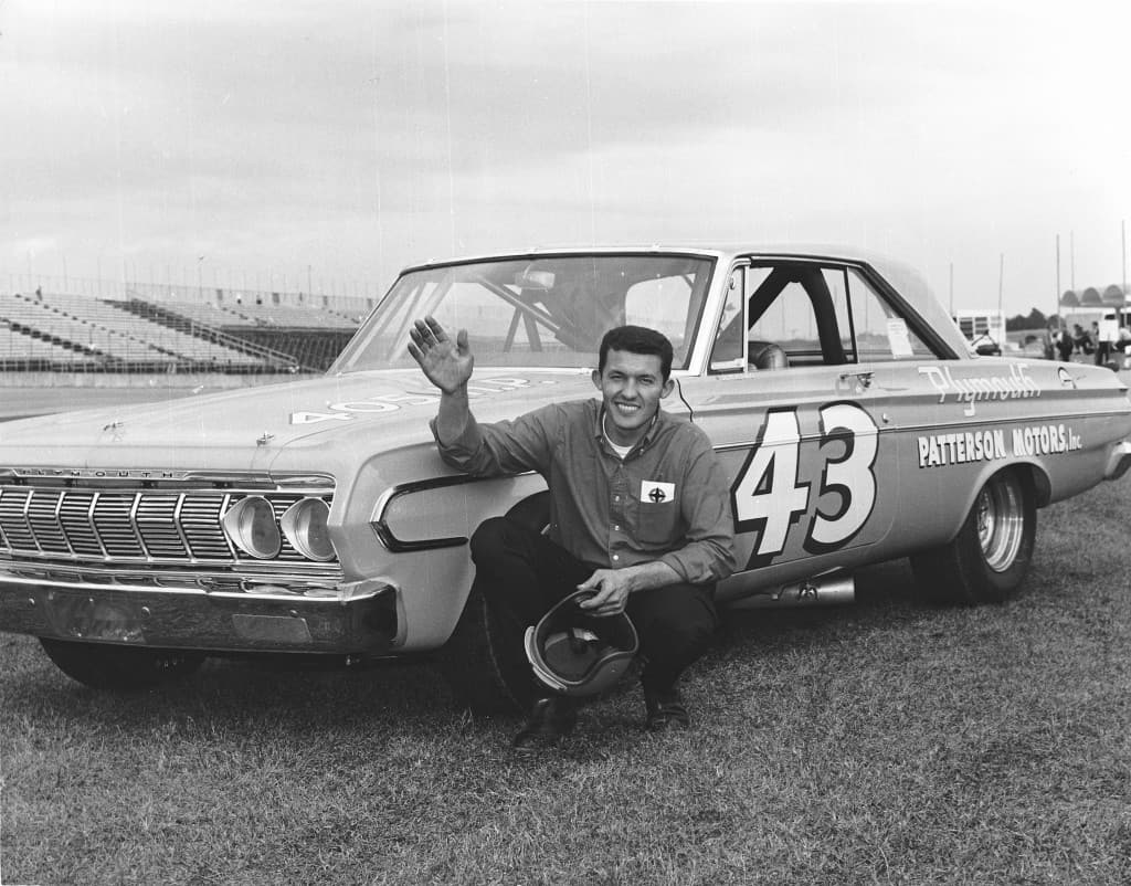 Richard Petty seating outside of a Plymouth race car 43